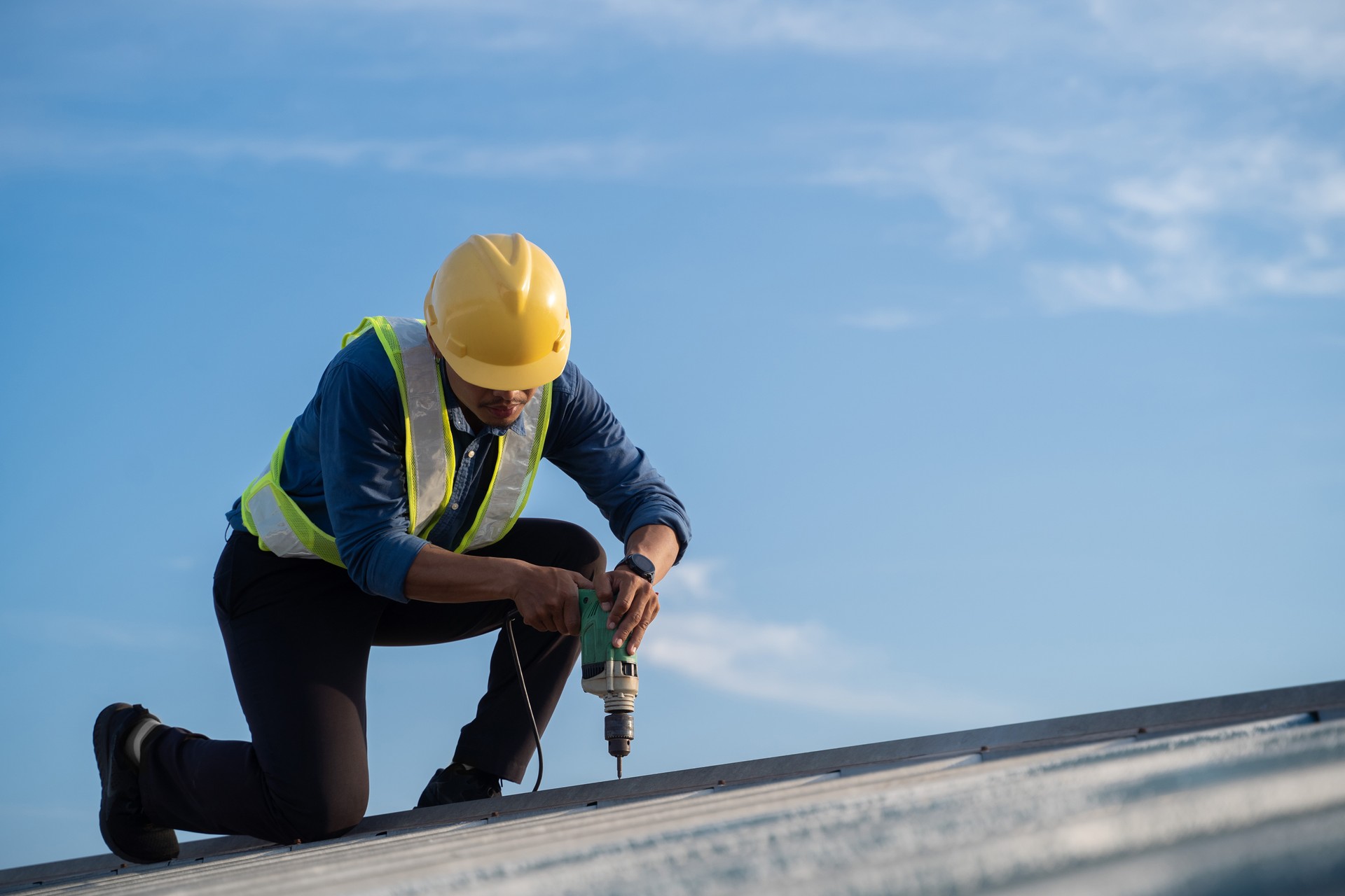 Worker repairing the roof on a construction site. Electric drill used on roof, Roof construction concept.